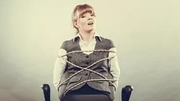 Person sitting on a chair tied with ropes, looking upwards.