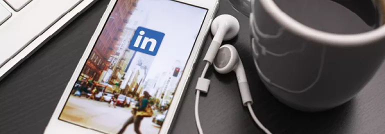 Smartphone with LinkedIn app next to a keyboard and coffee cup.